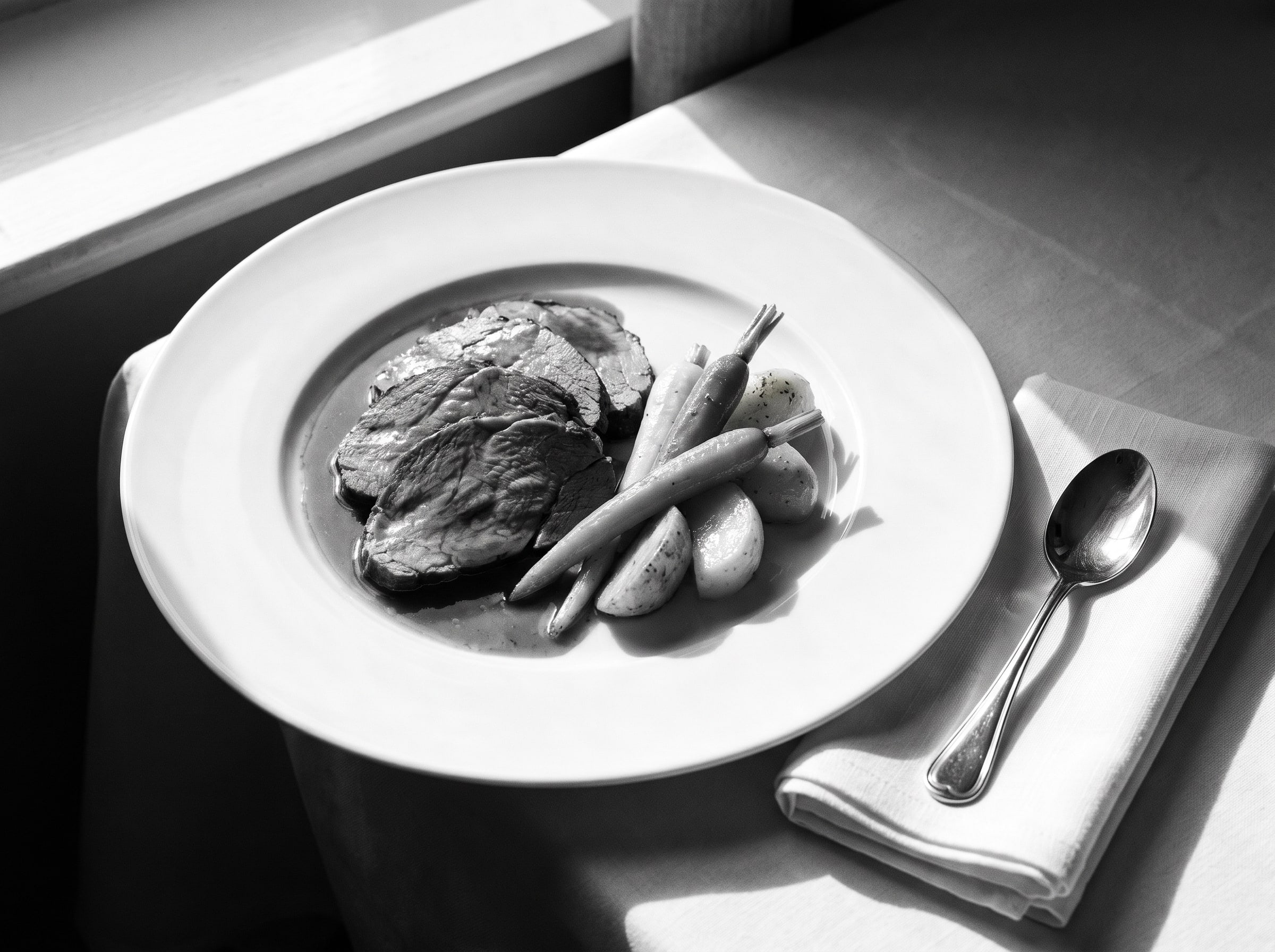 Aufgeschnittener Braten mit glänzendem Jus und gedrehtem Gemüse auf weissem Porzellan, Schwarzweiss-Aufnahme